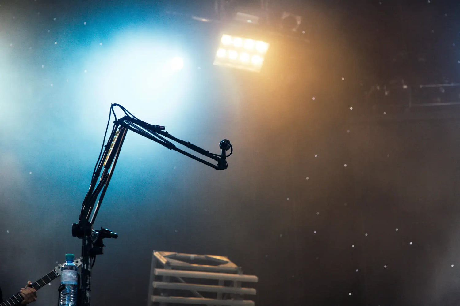 Black articulated microphone boom arm with a mounted condenser mic, positioned against stage lighting.