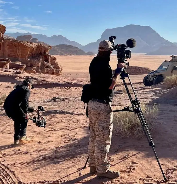 Black professional video camera mounted on a tripod in a desert setting.