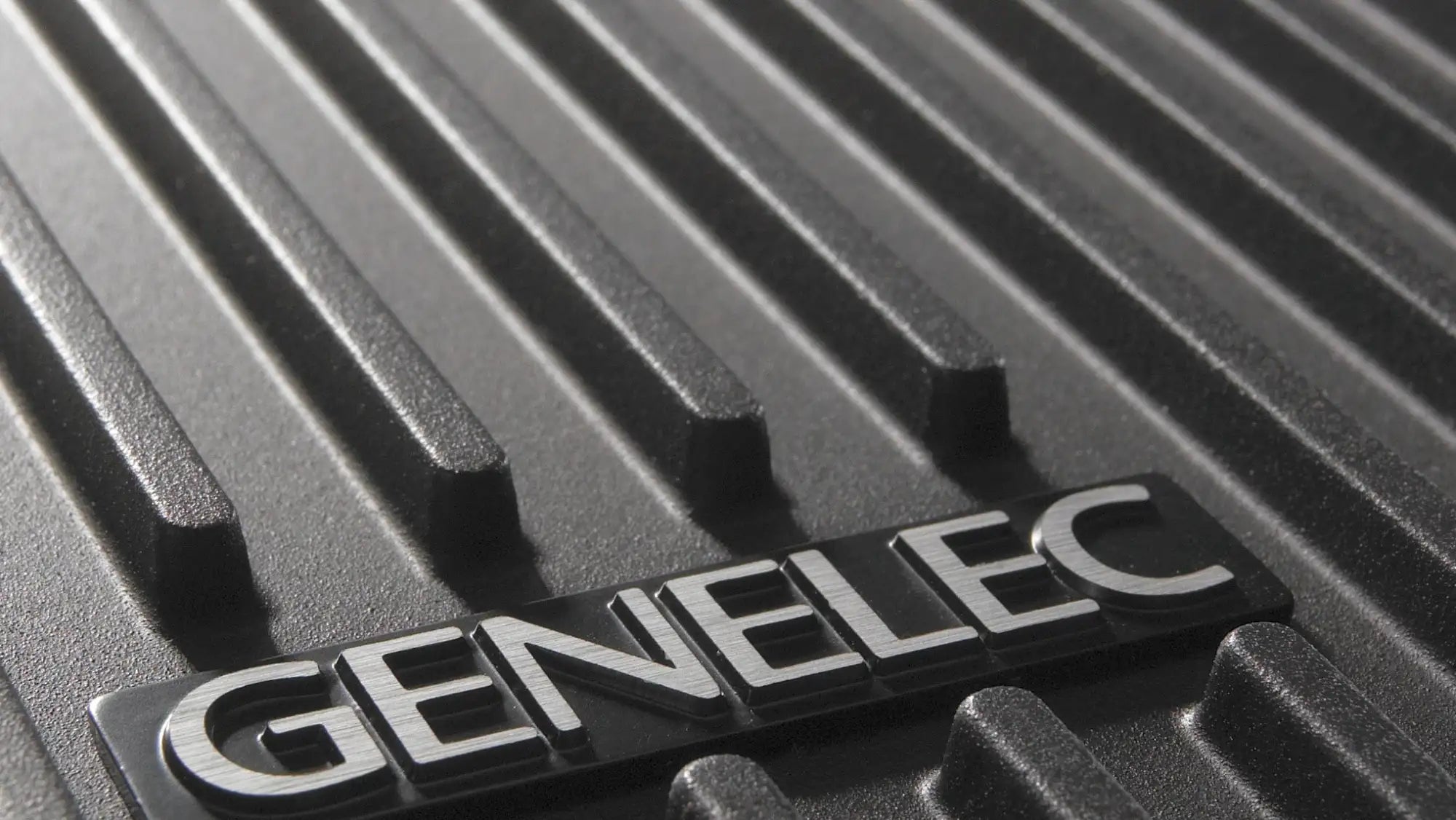 Black textured surface with a silver ’genelec’ logo plaque.