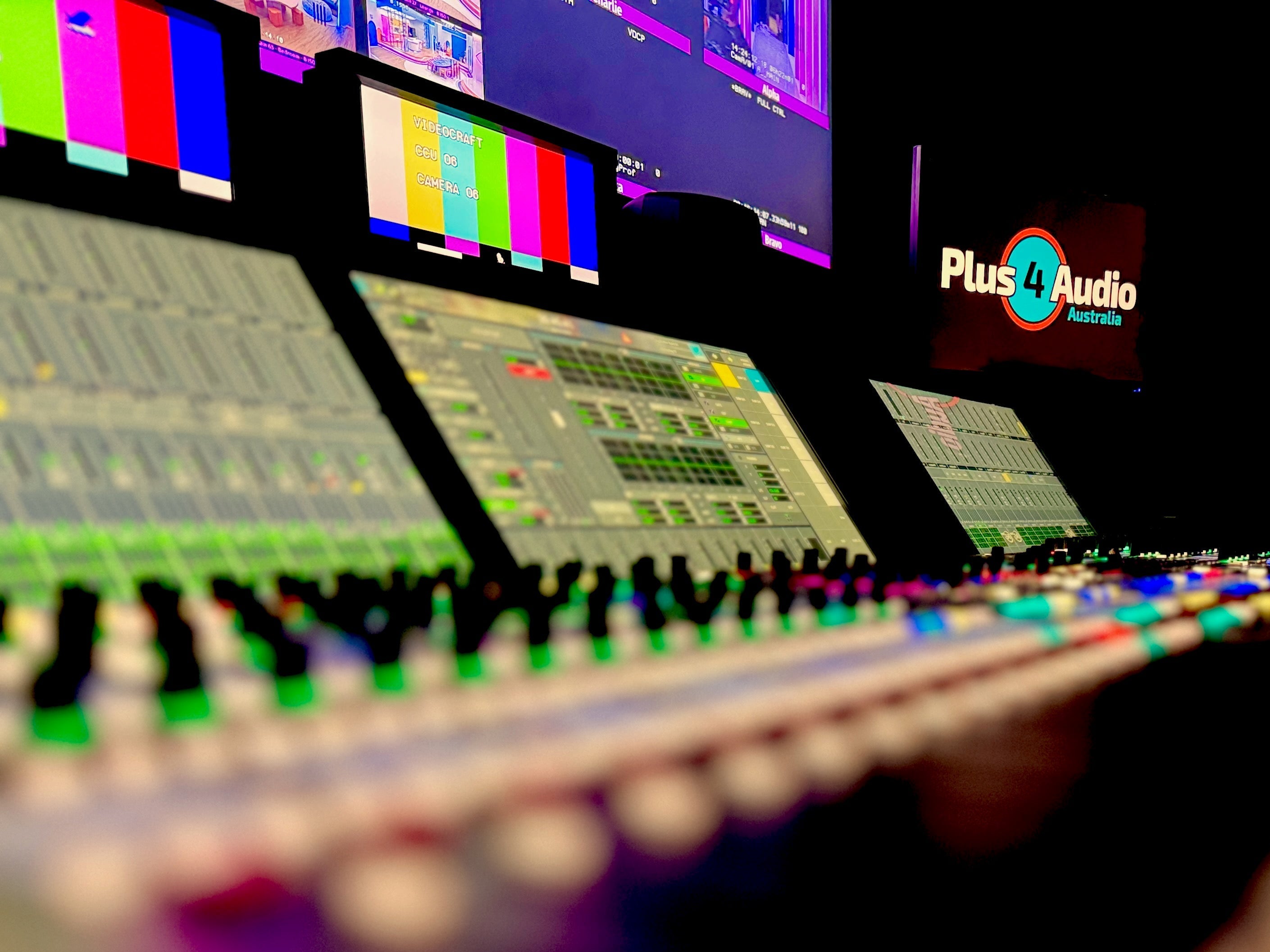 Audio mixing console with screens displaying colorful bars in a dark setting, featuring Plus4 Audio branding.