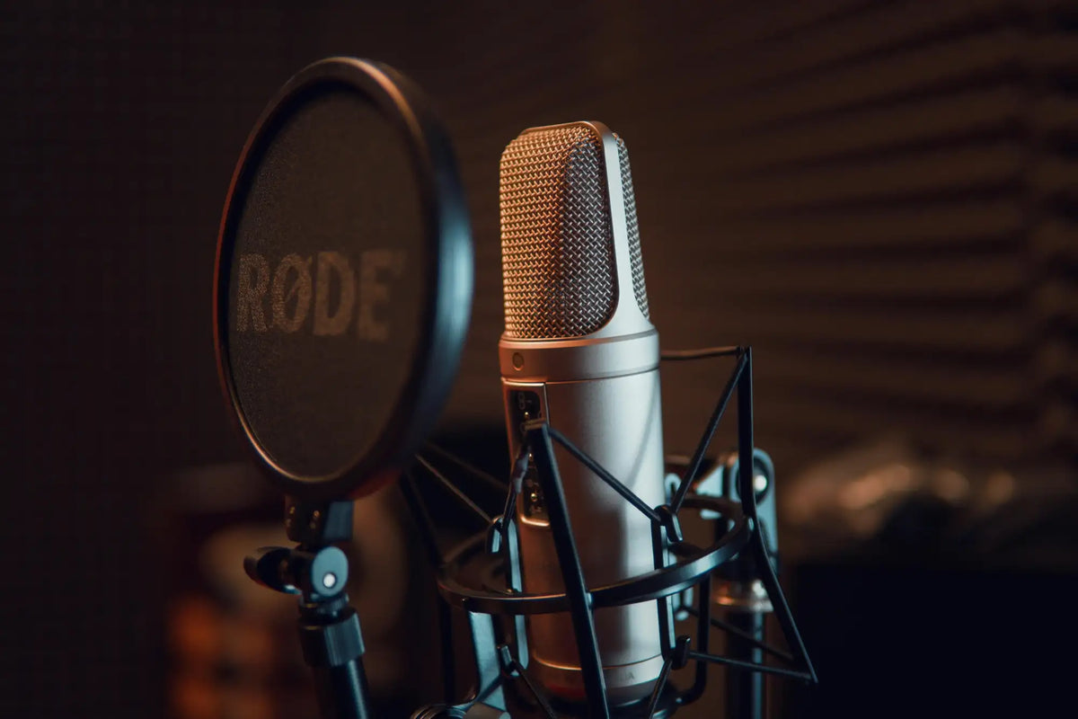 A sleek silver rode microphone with a gold mesh grille, mounted in a professional studio setup.